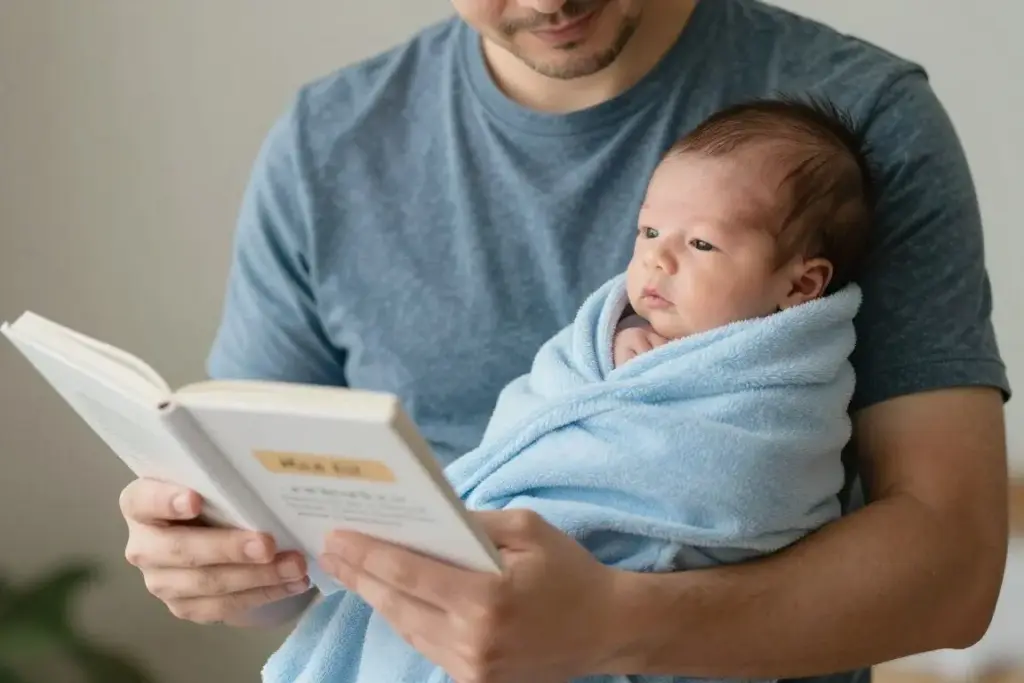 A father holding his newborn baby boy while looking at a baby name book