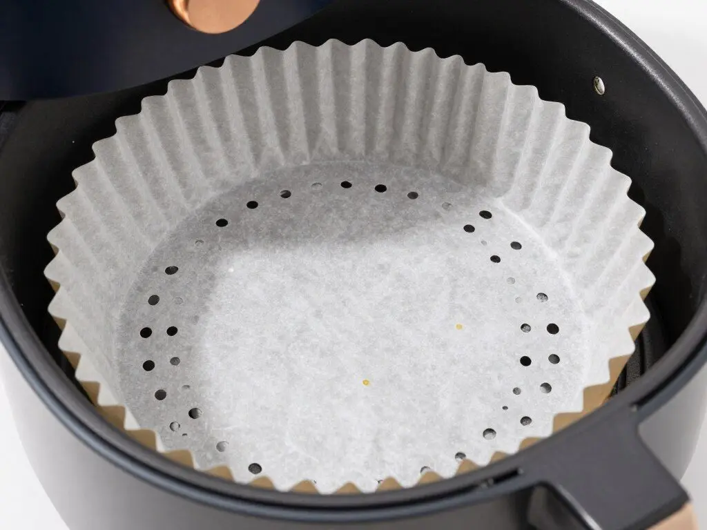 Perforated parchment paper liner being placed in air fryer basket