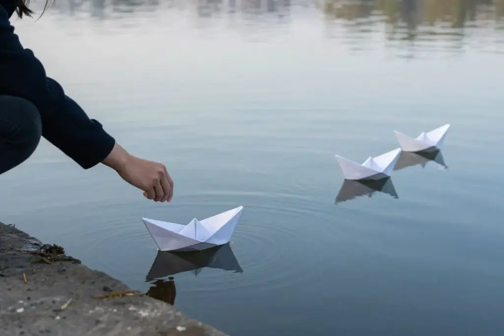 Person letting go of paper boats in water symbolizing release