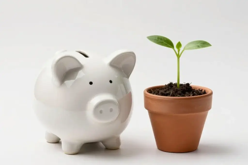 A ceramic savings jar with a few coins beside a growing green sprout in a small terracotta pot