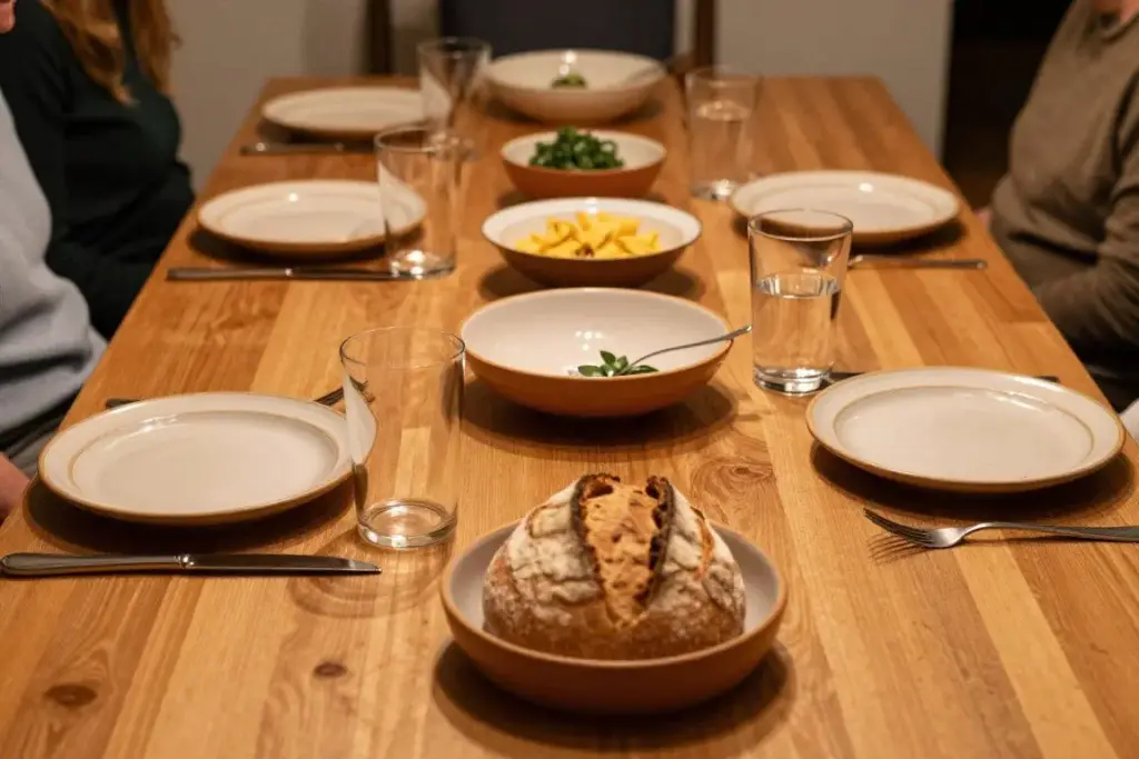 A dining table laid with ceramic bowls, fresh bread, and salad, ready for a convivial family supper