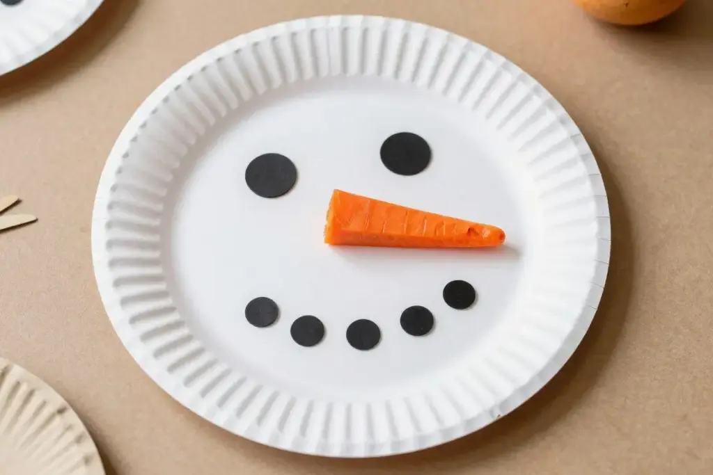 Paper plate snowman craft with orange carrot nose and button eyes